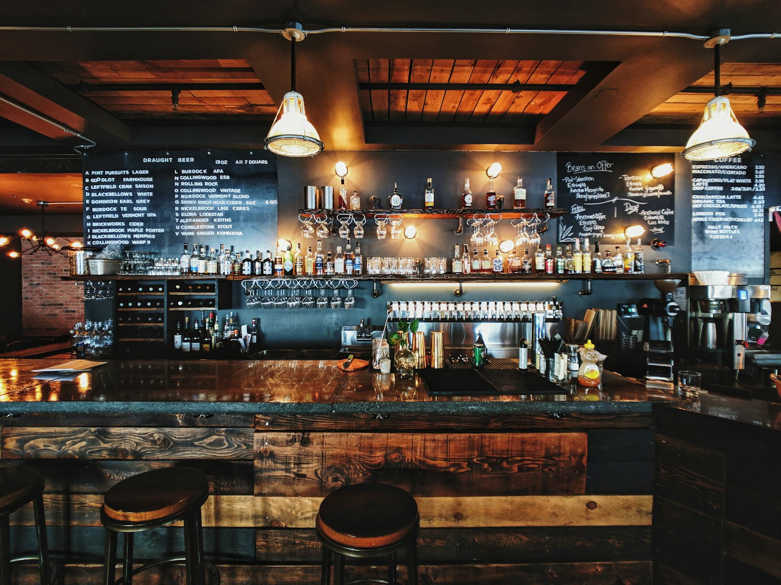 Balcão de bar à noite com banquetas e prateleira de garrafas
